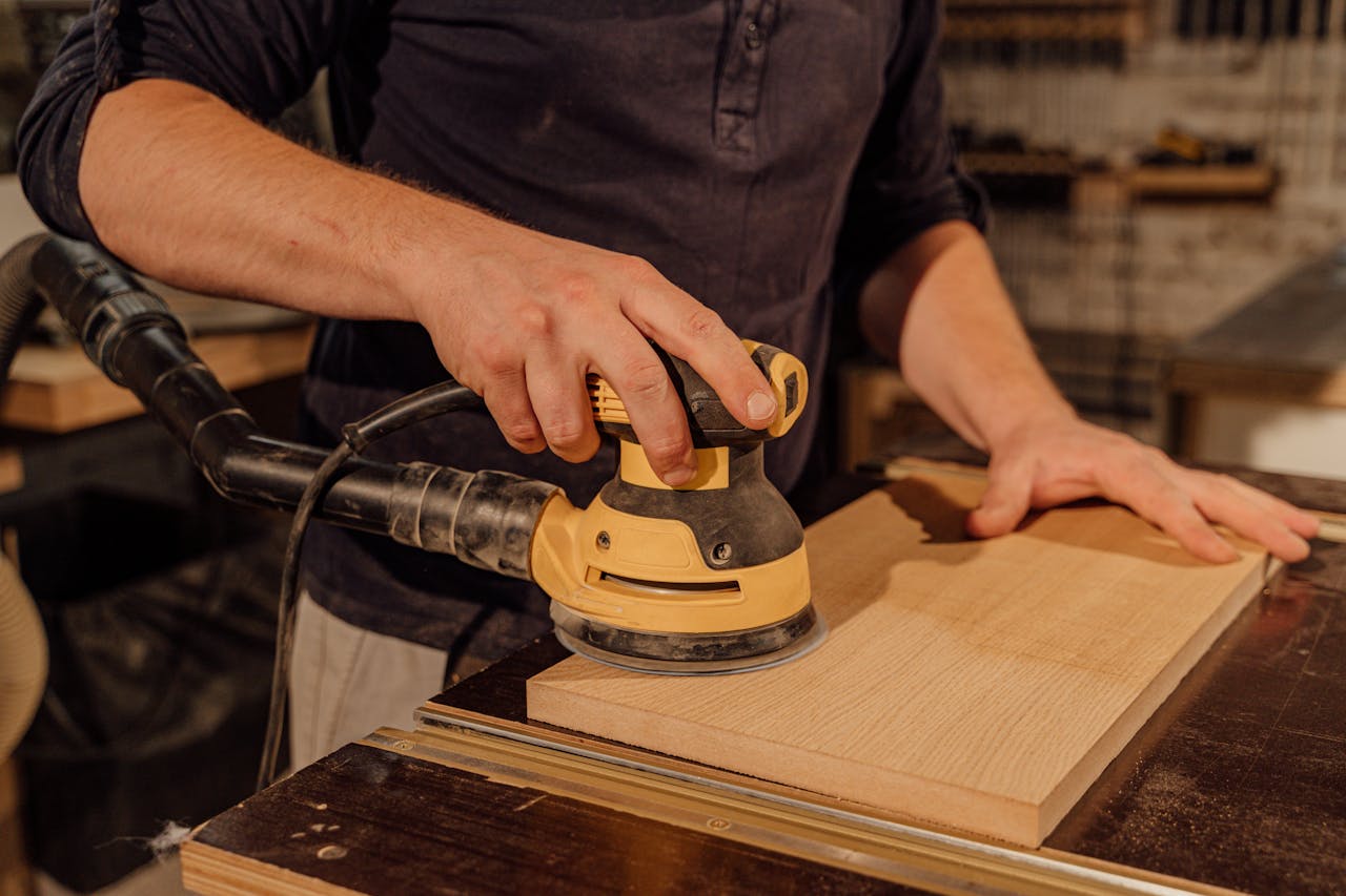 Carpenter using an electric sander on a wooden board in a workshop, showcasing craftsmanship.